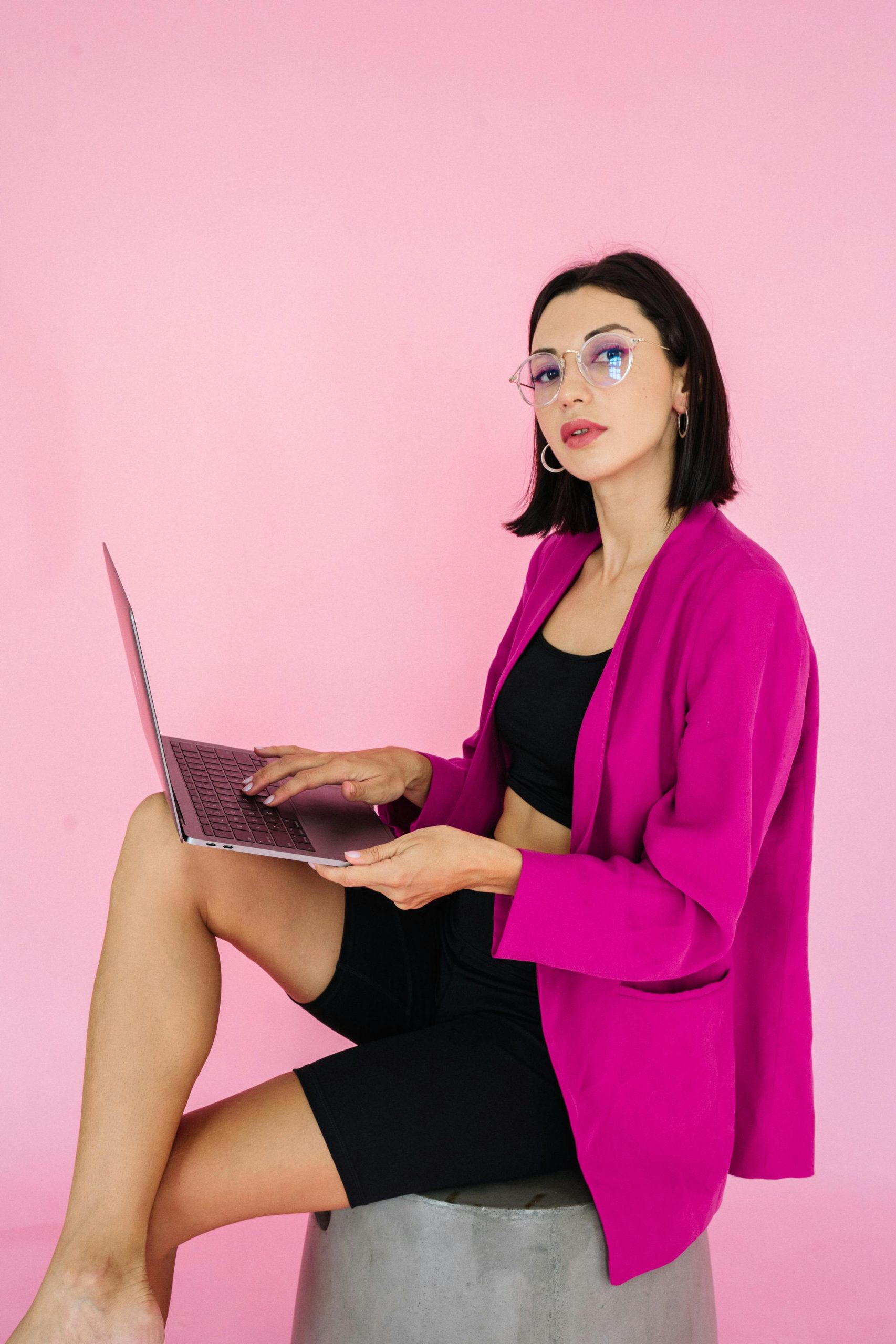 Confident woman in pink blazer using a laptop, embodying modern digital nomad style.